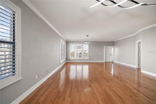 unfurnished living room with ornamental molding, light wood-type flooring, a textured wall, and baseboards