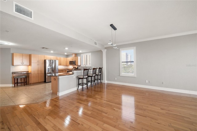 kitchen with a breakfast bar, stainless steel appliances, dark countertops, visible vents, and light wood-style flooring