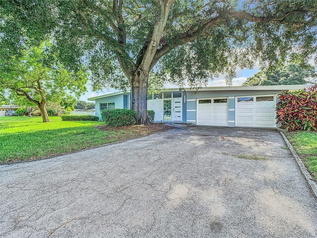 single story home with aphalt driveway, an attached garage, and a front lawn