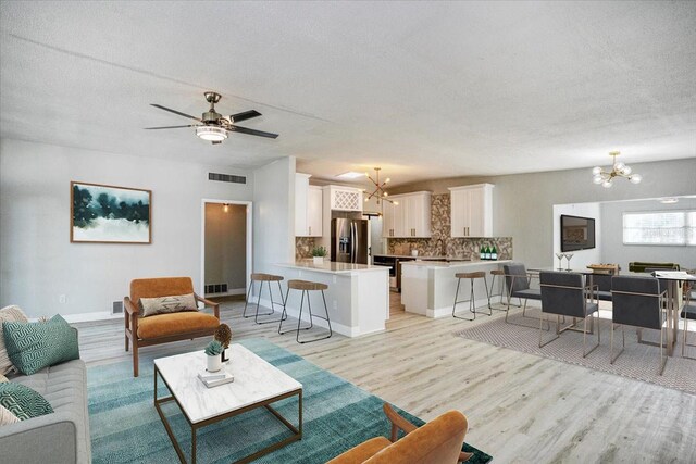 living room featuring light wood-type flooring, ceiling fan with notable chandelier, and a textured ceiling