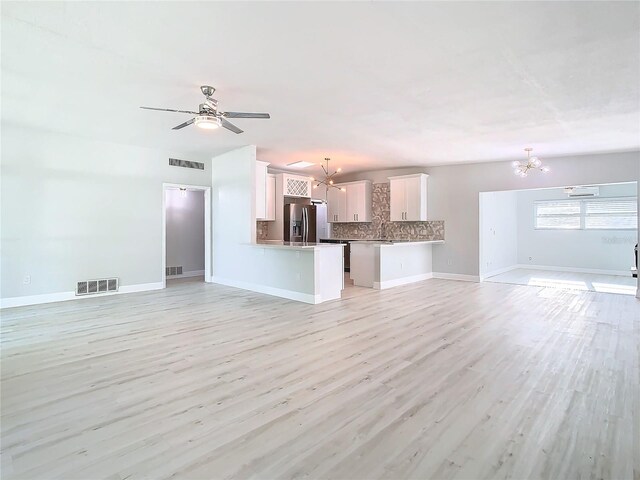 unfurnished living room featuring sink, light wood-type flooring, and ceiling fan with notable chandelier