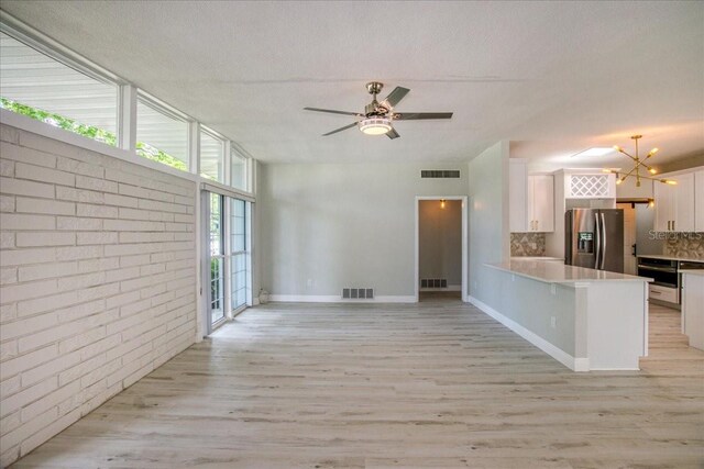 interior space with brick wall, ceiling fan with notable chandelier, a textured ceiling, and light hardwood / wood-style flooring