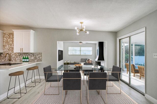 dining space featuring sink, a textured ceiling, ceiling fan with notable chandelier, and light wood-type flooring