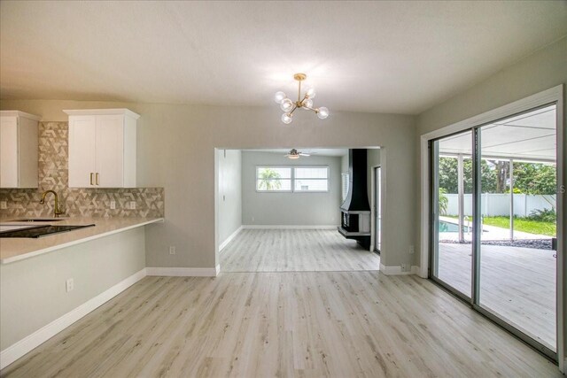 unfurnished dining area with ceiling fan with notable chandelier, sink, and light wood-type flooring