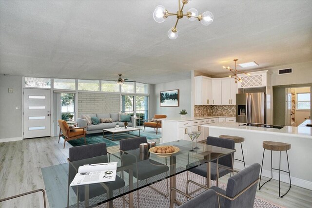 dining room with ceiling fan with notable chandelier, light hardwood / wood-style flooring, and a textured ceiling