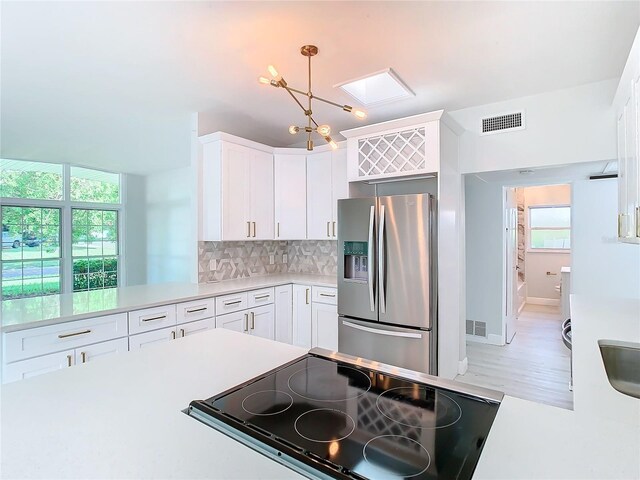 kitchen with a chandelier, hanging light fixtures, decorative backsplash, light wood-type flooring, and stainless steel fridge