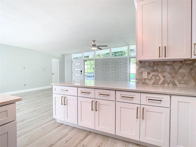 kitchen featuring light countertops, decorative backsplash, a ceiling fan, light wood-type flooring, and baseboards