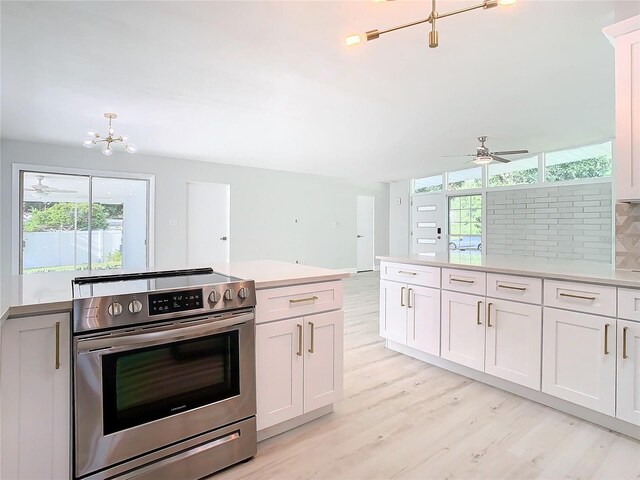 kitchen with white cabinetry, light hardwood / wood-style flooring, backsplash, stainless steel electric range, and ceiling fan with notable chandelier