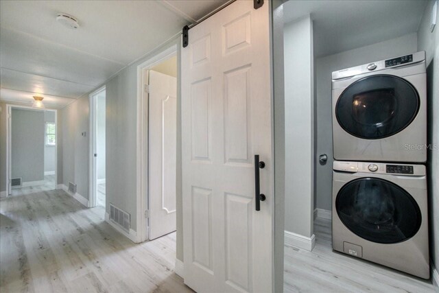 clothes washing area with light hardwood / wood-style flooring, stacked washer and dryer, and a barn door