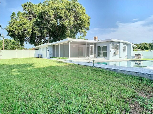 back of house featuring cooling unit, a fenced backyard, a sunroom, a lawn, and a fenced in pool