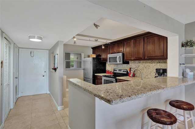 kitchen with a kitchen breakfast bar, tasteful backsplash, kitchen peninsula, light tile patterned floors, and stainless steel appliances