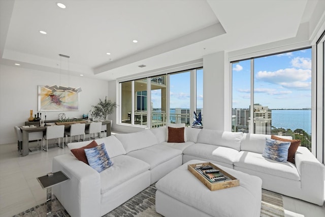 living room featuring light tile patterned flooring, a raised ceiling, and a water view