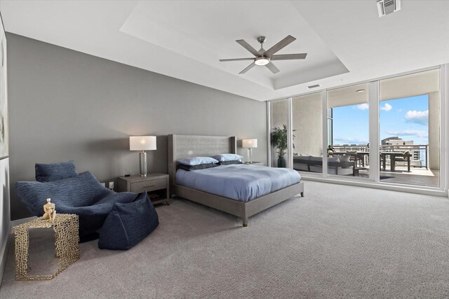 carpeted bedroom with ceiling fan, a raised ceiling, and access to exterior