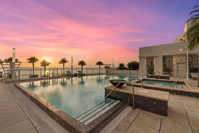 pool at dusk with a community hot tub and a patio