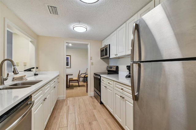 kitchen featuring light hardwood / wood-style flooring, sink, white cabinetry, stainless steel appliances, and light stone countertops