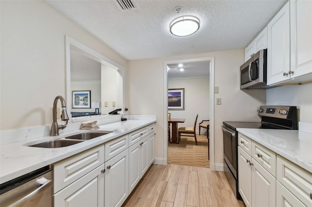 kitchen featuring appliances with stainless steel finishes, light wood-type flooring, light stone counters, sink, and white cabinetry