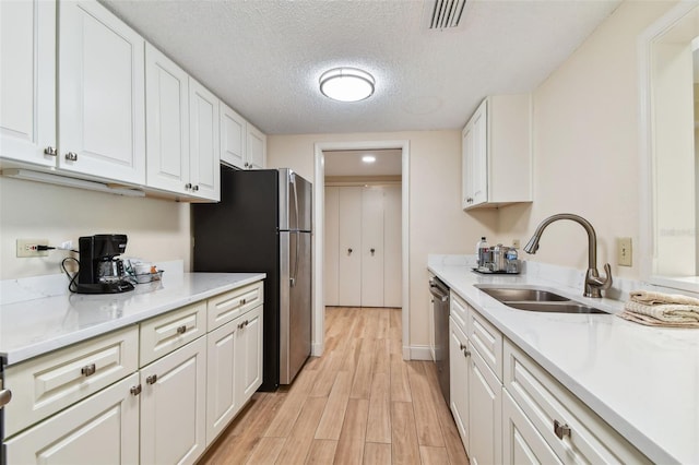 kitchen with sink, white cabinetry, stainless steel appliances, and light hardwood / wood-style floors