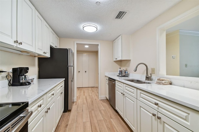 kitchen with light hardwood / wood-style flooring, stainless steel appliances, a textured ceiling, white cabinets, and sink