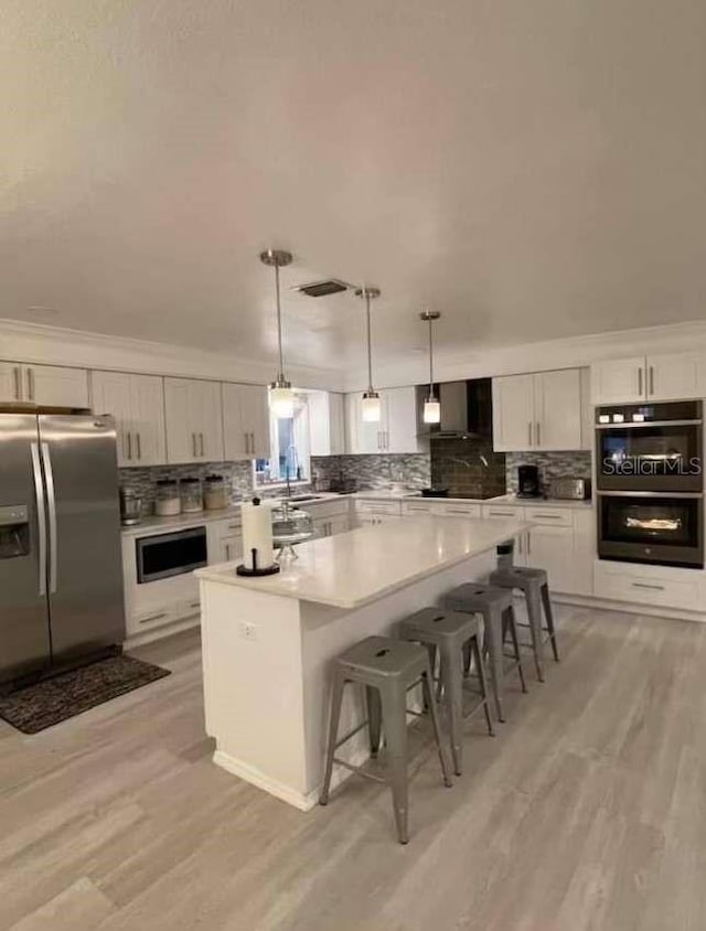 kitchen with hanging light fixtures, stainless steel refrigerator with ice dispenser, a center island, a breakfast bar area, and light hardwood / wood-style floors