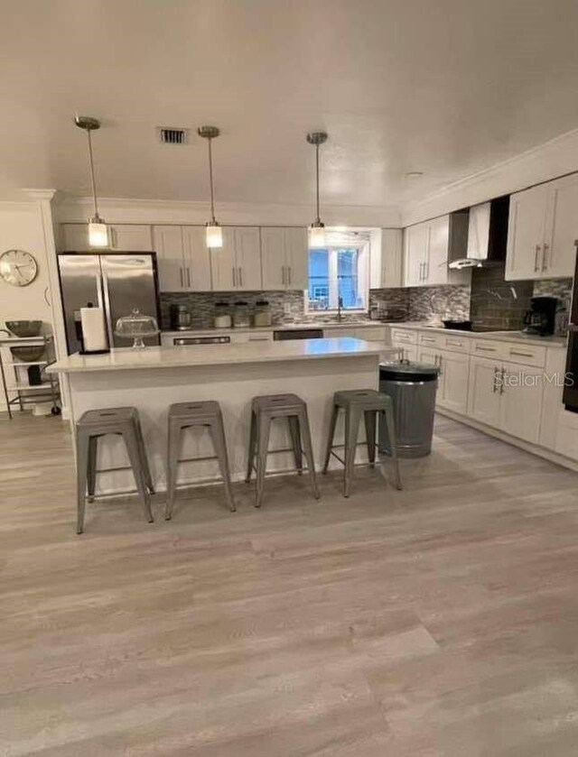 kitchen with light hardwood / wood-style floors, stainless steel fridge with ice dispenser, a kitchen island, and wall chimney exhaust hood