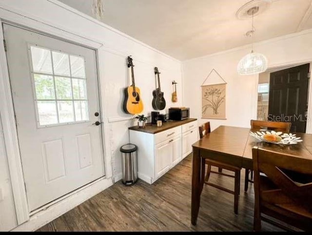 interior space featuring ornamental molding, dark hardwood / wood-style flooring, hanging light fixtures, and white cabinets