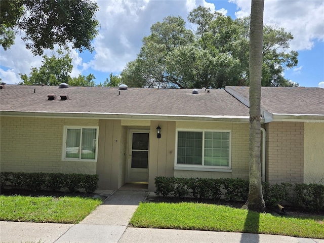 view of front of home featuring brick siding, roof with shingles, and a front yard