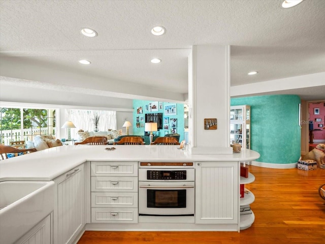 kitchen featuring oven, a textured ceiling, kitchen peninsula, and light wood-type flooring