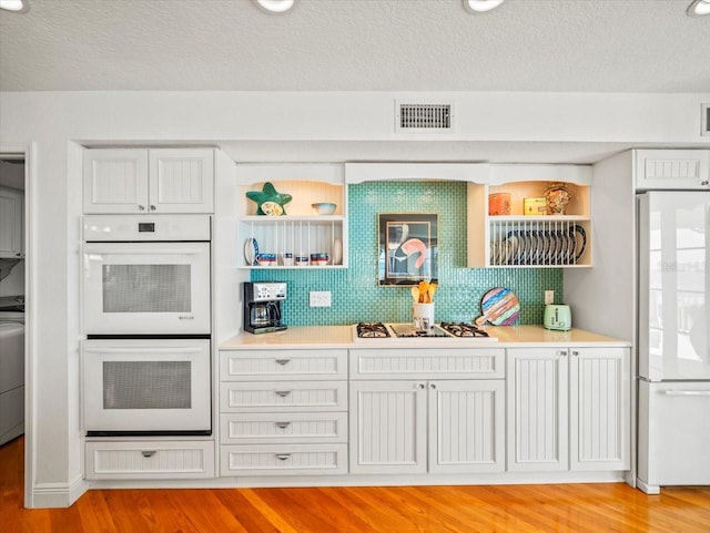 bar with tasteful backsplash, white appliances, light hardwood / wood-style floors, washer / clothes dryer, and white cabinetry