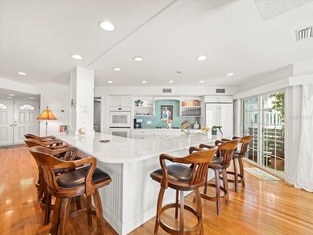 kitchen with a breakfast bar, light hardwood / wood-style flooring, a textured ceiling, white cabinets, and white double oven