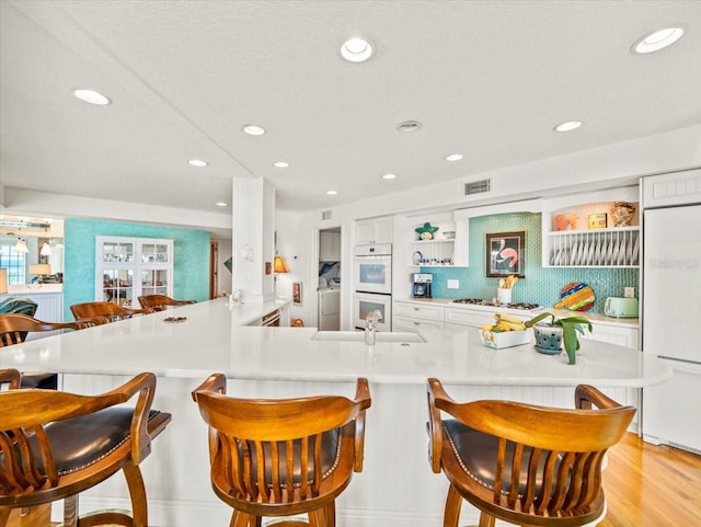 kitchen with white appliances, kitchen peninsula, light hardwood / wood-style floors, a kitchen breakfast bar, and sink