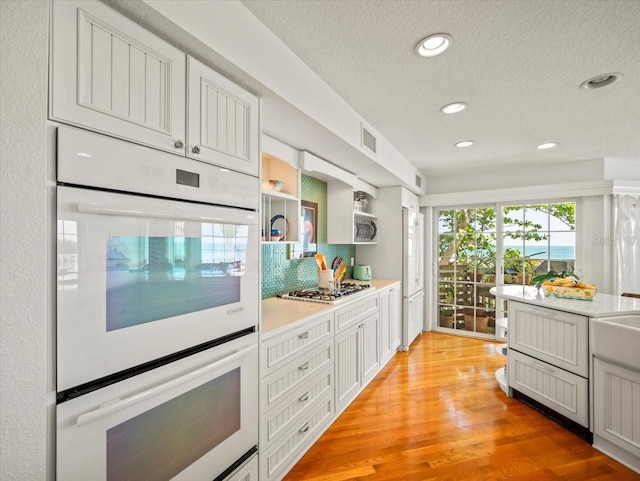 kitchen with tasteful backsplash, white double oven, gas stovetop, light wood-type flooring, and a textured ceiling