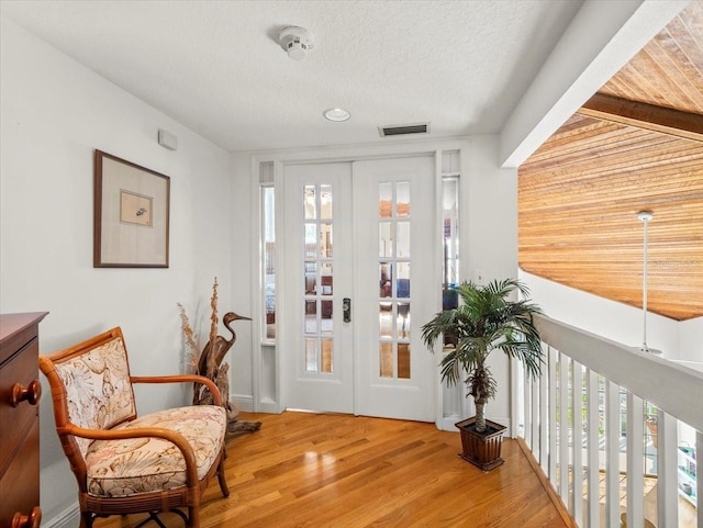 entrance foyer featuring a textured ceiling, wood-type flooring, french doors, and beamed ceiling