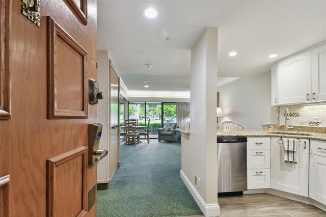 kitchen with stainless steel dishwasher, white cabinets, sink, light colored carpet, and light stone countertops