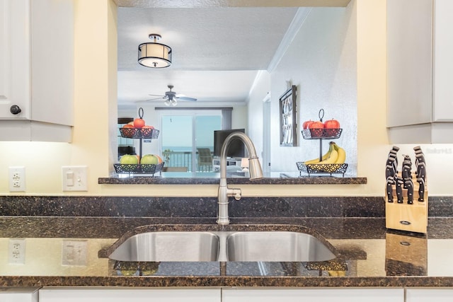 kitchen with dark stone countertops, white cabinetry, sink, and ornamental molding