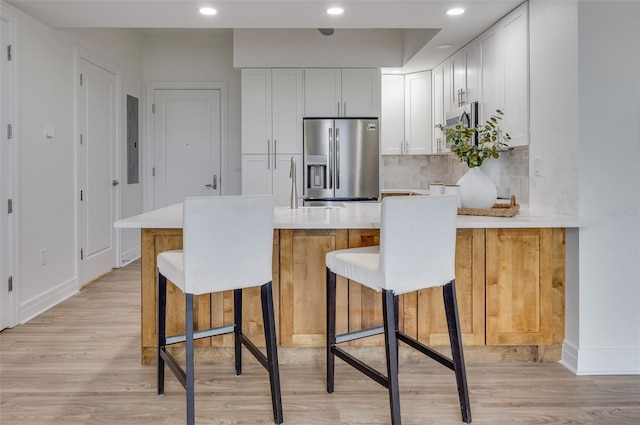 kitchen with white cabinetry, decorative backsplash, stainless steel fridge with ice dispenser, a kitchen bar, and light hardwood / wood-style flooring