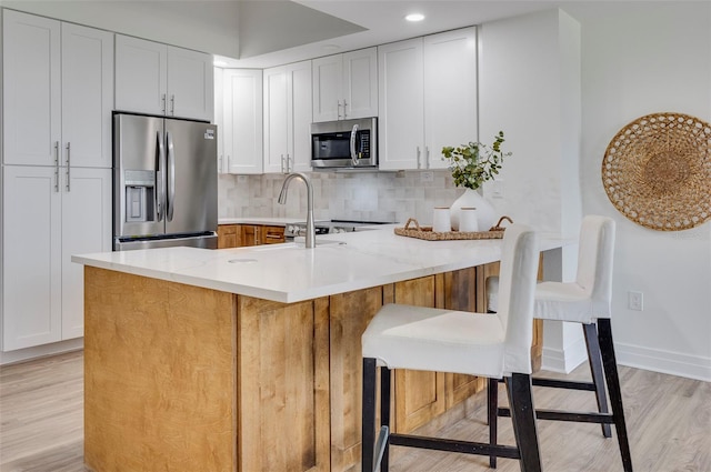 kitchen featuring appliances with stainless steel finishes, light hardwood / wood-style flooring, tasteful backsplash, and light stone counters