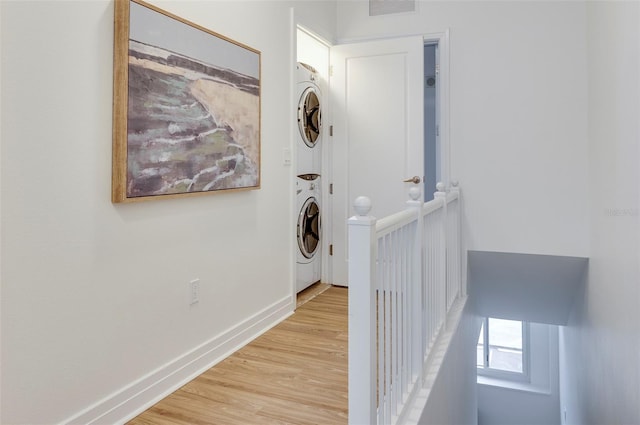 hallway with stacked washer and clothes dryer and light wood-type flooring