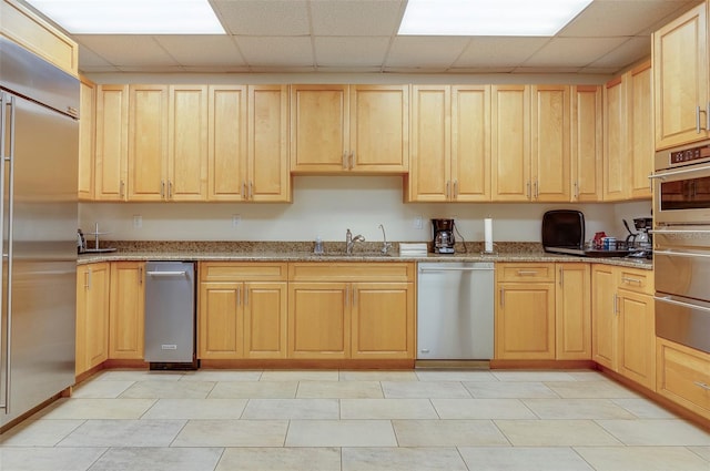 kitchen with a drop ceiling, light tile patterned floors, light stone counters, and stainless steel appliances