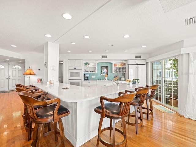 kitchen featuring white cabinets, a breakfast bar, light wood-type flooring, and white double oven