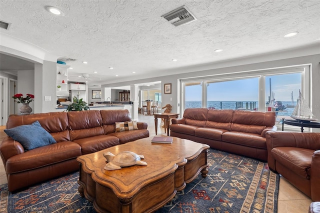 tiled living room featuring a textured ceiling and a water view