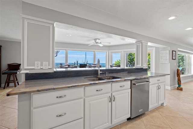 kitchen with sink, light tile patterned floors, stainless steel dishwasher, kitchen peninsula, and white cabinets