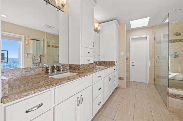 bathroom with tile patterned flooring, a skylight, a water view, vanity, and walk in shower