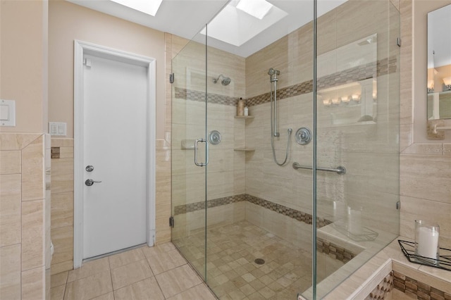 bathroom with a skylight, a shower with door, and tile walls