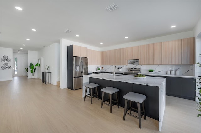 kitchen featuring a breakfast bar area, light stone counters, light hardwood / wood-style flooring, appliances with stainless steel finishes, and an island with sink