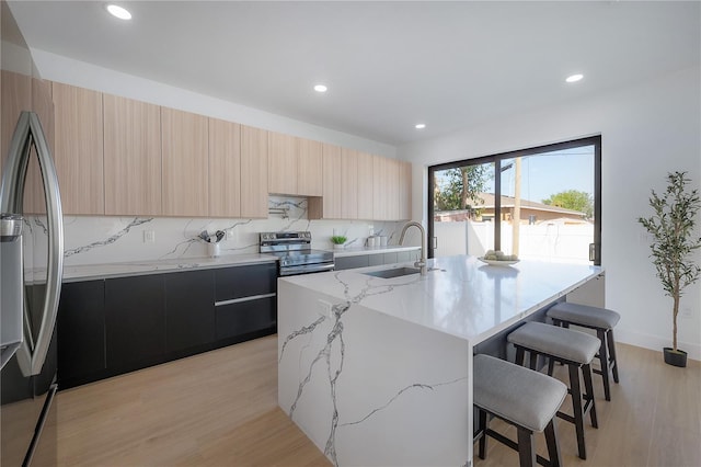 kitchen featuring an island with sink, sink, a breakfast bar area, light stone counters, and stainless steel appliances