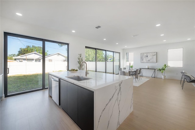 kitchen featuring dishwasher, sink, a kitchen island with sink, light stone countertops, and a healthy amount of sunlight