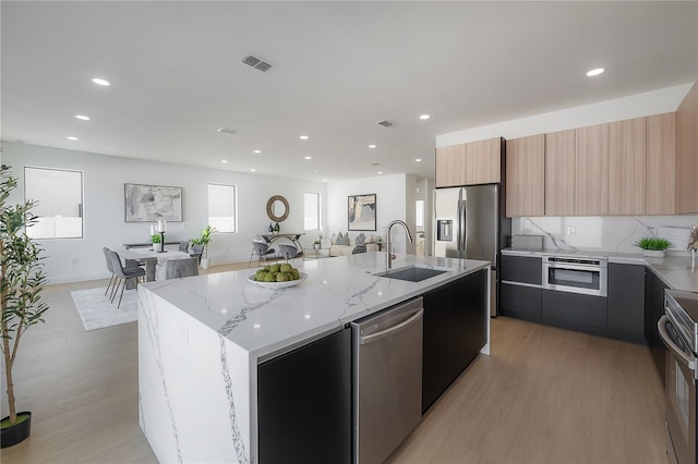 kitchen featuring light stone countertops, an island with sink, appliances with stainless steel finishes, and sink