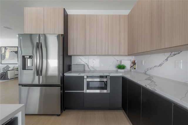 kitchen with light stone counters, tasteful backsplash, light brown cabinets, and appliances with stainless steel finishes