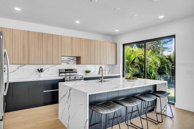 kitchen featuring a sink, appliances with stainless steel finishes, light brown cabinets, light stone countertops, and modern cabinets