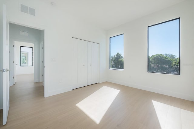 unfurnished bedroom featuring a closet, visible vents, baseboards, and light wood-style floors